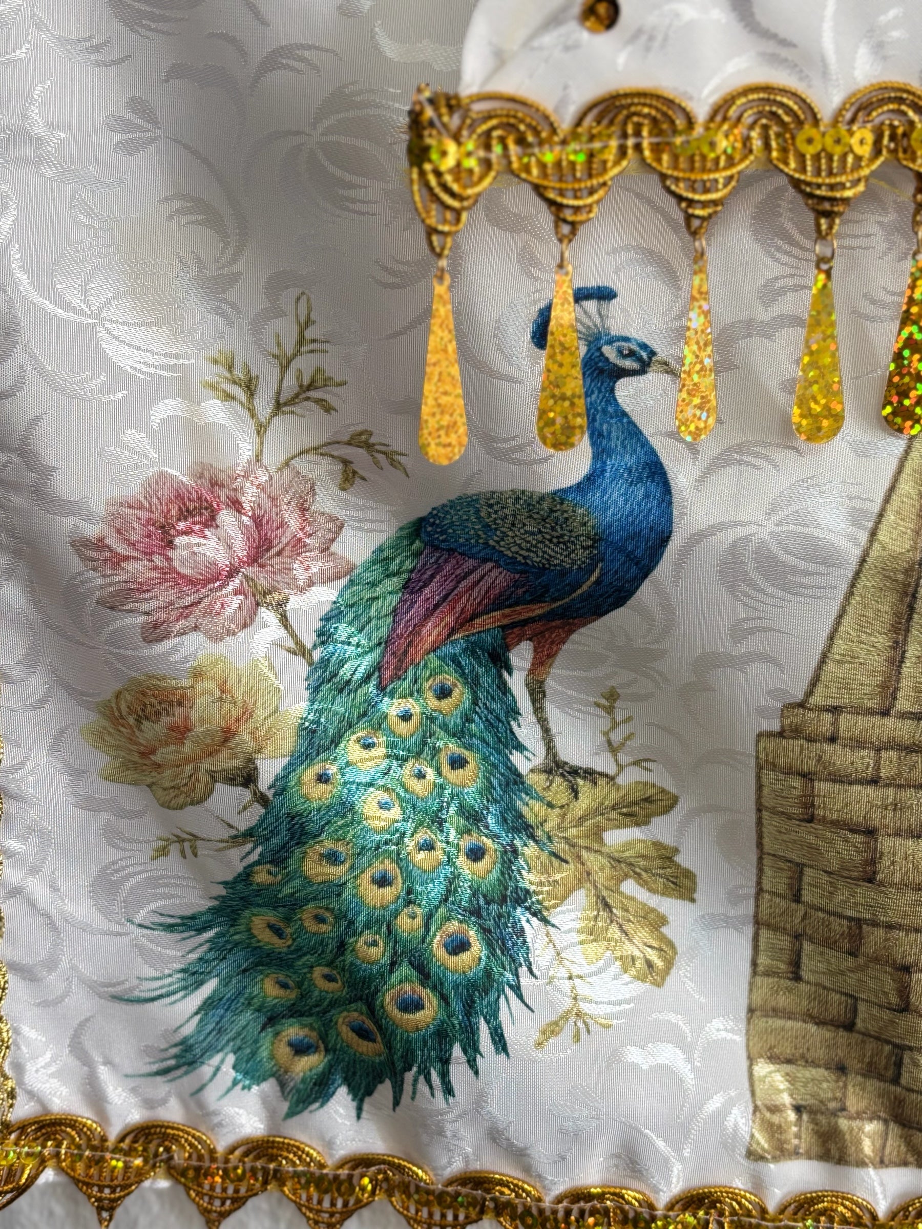 Milan Geschenk e.K Wandbehang mit Pfauenmotiv, weißem Textil, Goldpailletten und funkelnden tropfenförmigen Anhängern.